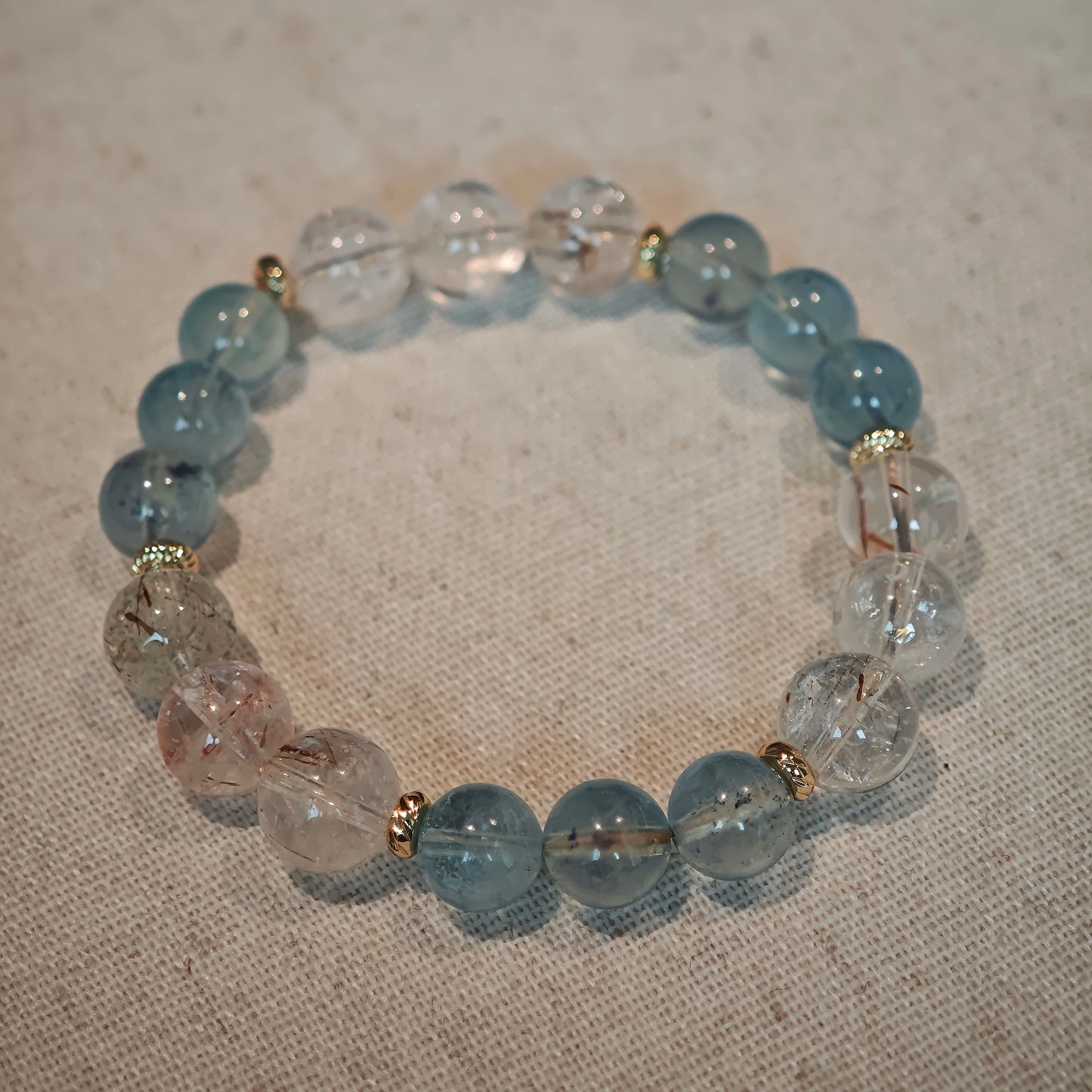 A cool aquamarine strand glows warmer with rutile and gold, mirroring a sunrise over water.