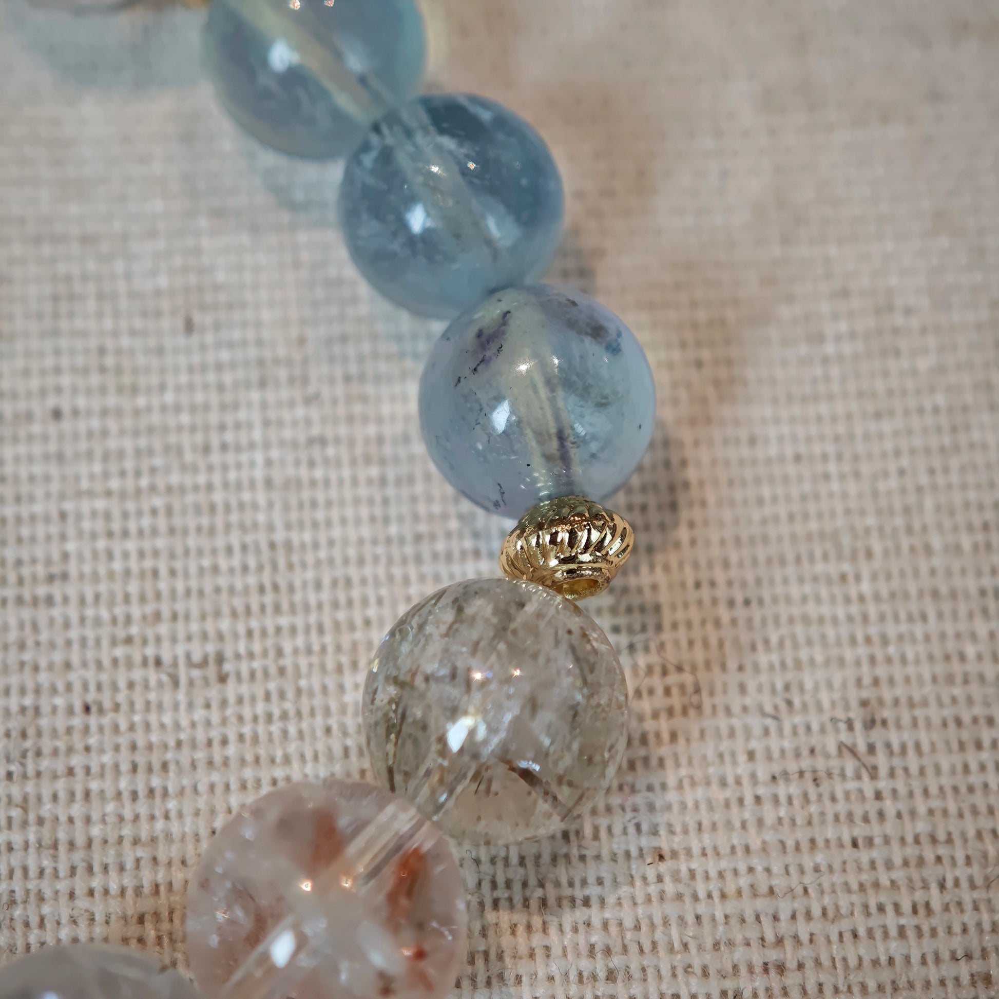 Cool aquamarine pools and warm rutile threads are circled by elegant gold separators, creating a layered tide of color.