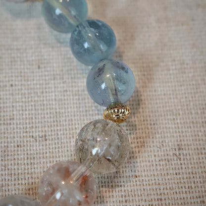 Cool aquamarine pools and warm rutile threads are circled by elegant gold separators, creating a layered tide of color.