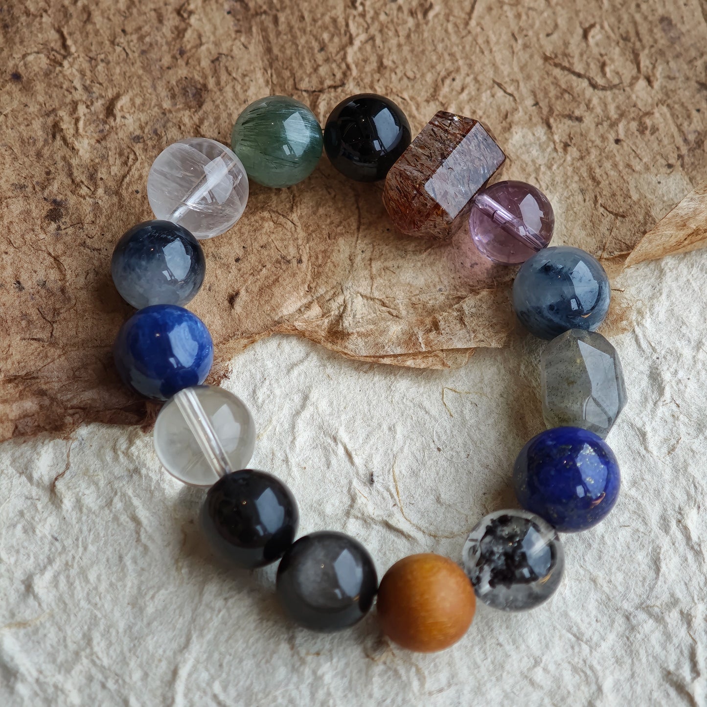 A mystic bracelet woven from Black Gold Super Seven, Herkimer diamonds, clear quartz, sandalwood, amethyst, silver obsidian, white phantom quartz, and kyanite in cool blue-grey.