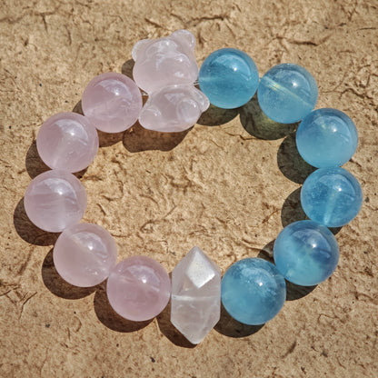 This bracelet consists of rose quartz and aquamarine. The bracelet features a bead pendant and a rhombic spacer, both of which are made of rose quartz. The bracelet is a combination of pink and blue colors.