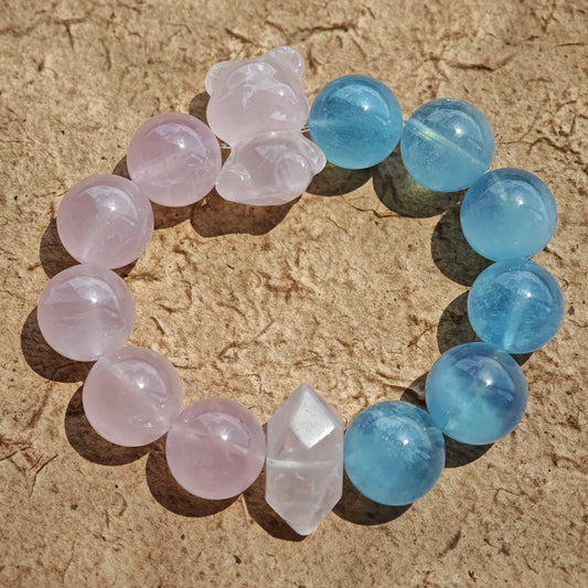 This bracelet consists of rose quartz and aquamarine. The bracelet features a bead pendant and a rhombic spacer, both of which are made of rose quartz. The bracelet is a combination of pink and blue colors.