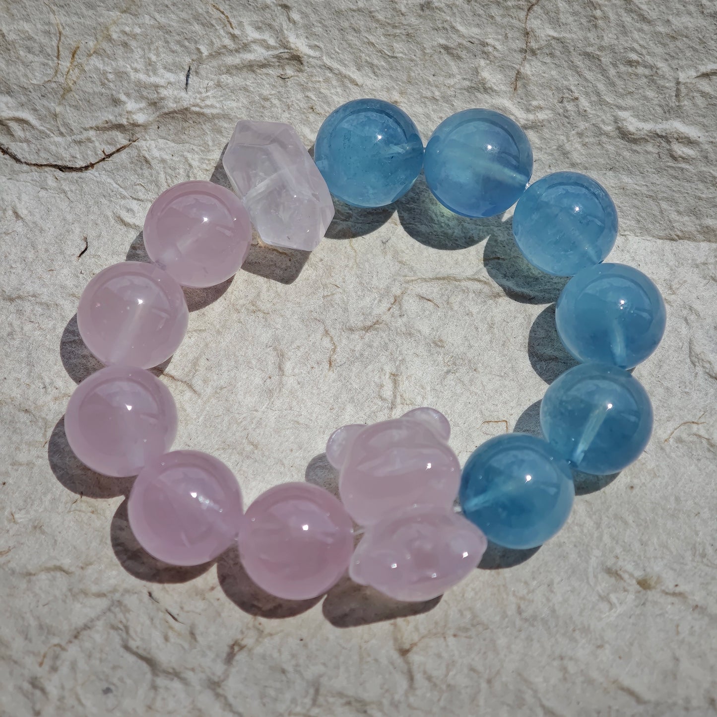 This bracelet consists of rose quartz and aquamarine. The bracelet features a bead pendant and a rhombic spacer, both of which are made of rose quartz. The bracelet is a combination of pink and blue colors.