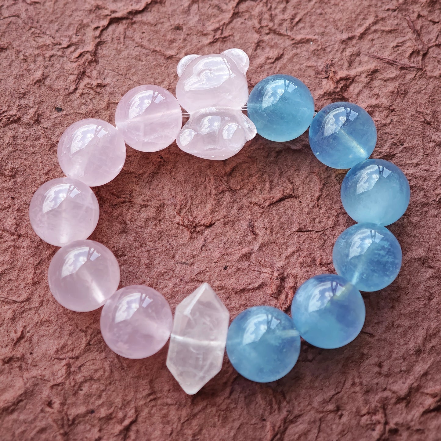 This bracelet consists of rose quartz and aquamarine. The bracelet features a bead pendant and a rhombic spacer, both of which are made of rose quartz. The bracelet is a combination of pink and blue colors.