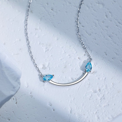 Crafted from polished S925 Sterling Silver, this necklace features a delicate 2.4cm curved bar pendant adorned with shimmering Blue Zircons to mimic a gentle, confident smile. The minimalist design is suspended on an adjustable 40cm clavicle chain, offering a mirror-like finish and a sophisticated touch of quiet luxury.
