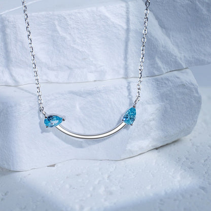 Crafted from polished S925 Sterling Silver, this necklace features a delicate 2.4cm curved bar pendant adorned with shimmering Blue Zircons to mimic a gentle, confident smile. The minimalist design is suspended on an adjustable 40cm clavicle chain, offering a mirror-like finish and a sophisticated touch of quiet luxury.