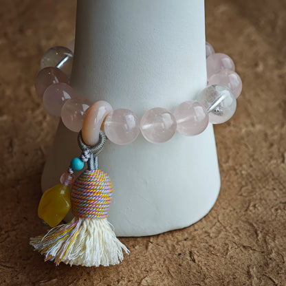 The bracelet pairs blushing quartz with ethereal blue needles, then sprinkles boho magic—amber star, agate bead, silky tassel.