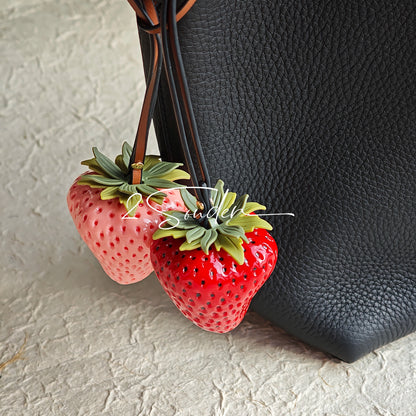 This is a simulated strawberry bag charm. The charm features a strawberry, the same size as a real strawberry, and is made of high-quality resin, giving it a very realistic appearance. It also has a leather cord attached, allowing it to be hung on bags, earphone cases, or used as a keychain. It's versatile and very cute.