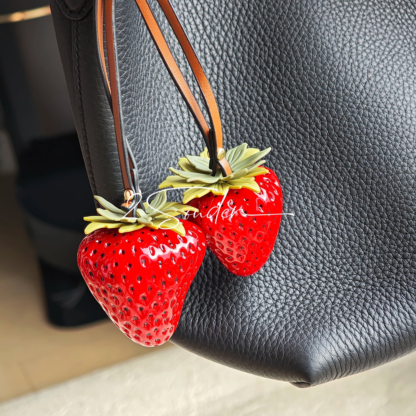 This is a simulated strawberry bag charm. The charm features a strawberry, the same size as a real strawberry, and is made of high-quality resin, giving it a very realistic appearance. It also has a leather cord attached, allowing it to be hung on bags, earphone cases, or used as a keychain. It's versatile and very cute.