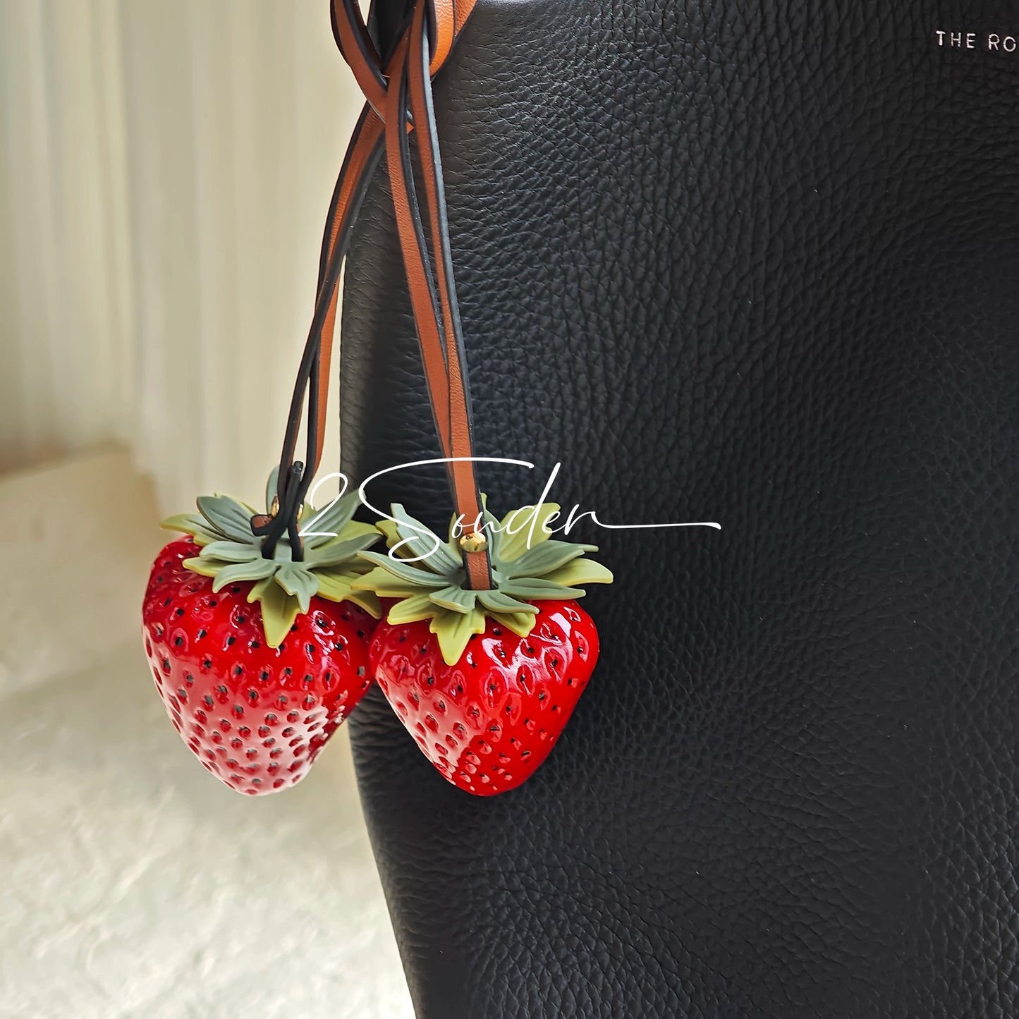 This is a simulated strawberry bag charm. The charm features a strawberry, the same size as a real strawberry, and is made of high-quality resin, giving it a very realistic appearance. It also has a leather cord attached, allowing it to be hung on bags, earphone cases, or used as a keychain. It's versatile and very cute.