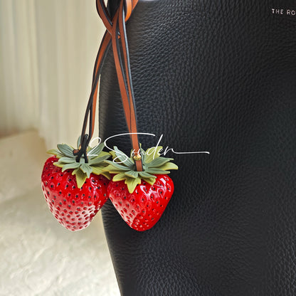 This is a simulated strawberry bag charm. The charm features a strawberry, the same size as a real strawberry, and is made of high-quality resin, giving it a very realistic appearance. It also has a leather cord attached, allowing it to be hung on bags, earphone cases, or used as a keychain. It's versatile and very cute.