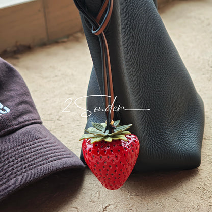 This is a simulated strawberry bag charm. The charm features a strawberry, the same size as a real strawberry, and is made of high-quality resin, giving it a very realistic appearance. It also has a leather cord attached, allowing it to be hung on bags, earphone cases, or used as a keychain. It's versatile and very cute.