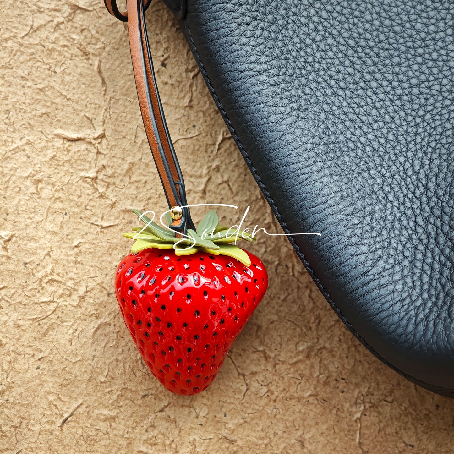 This is a simulated strawberry bag charm. The charm features a strawberry, the same size as a real strawberry, and is made of high-quality resin, giving it a very realistic appearance. It also has a leather cord attached, allowing it to be hung on bags, earphone cases, or used as a keychain. It's versatile and very cute.