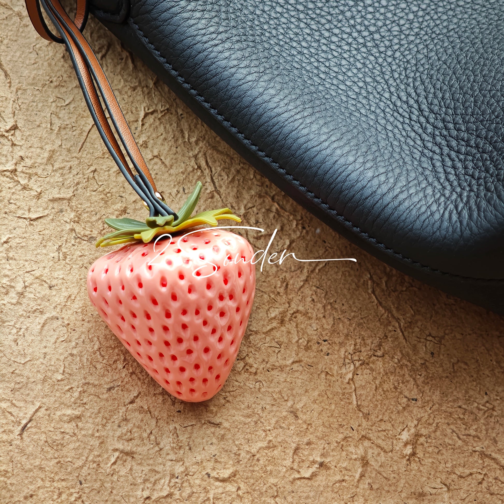 This is a simulated strawberry bag charm. The charm features a strawberry, the same size as a real strawberry, and is made of high-quality resin, giving it a very realistic appearance. It also has a leather cord attached, allowing it to be hung on bags, earphone cases, or used as a keychain. It's versatile and very cute.