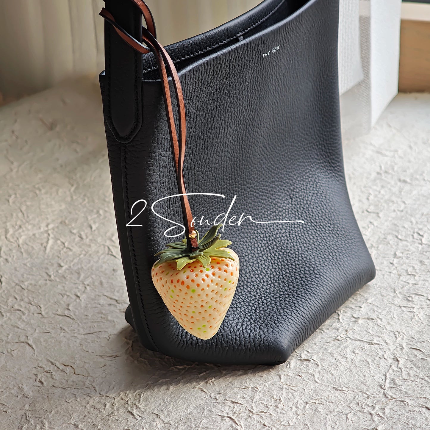 This is a simulated strawberry bag charm. The charm features a strawberry, the same size as a real strawberry, and is made of high-quality resin, giving it a very realistic appearance. It also has a leather cord attached, allowing it to be hung on bags, earphone cases, or used as a keychain. It's versatile and very cute.