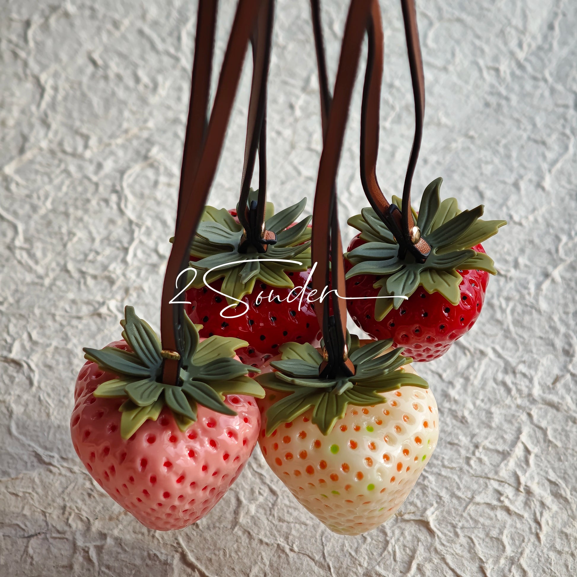 This is a simulated strawberry bag charm. The charm features a strawberry, the same size as a real strawberry, and is made of high-quality resin, giving it a very realistic appearance. It also has a leather cord attached, allowing it to be hung on bags, earphone cases, or used as a keychain. It's versatile and very cute.