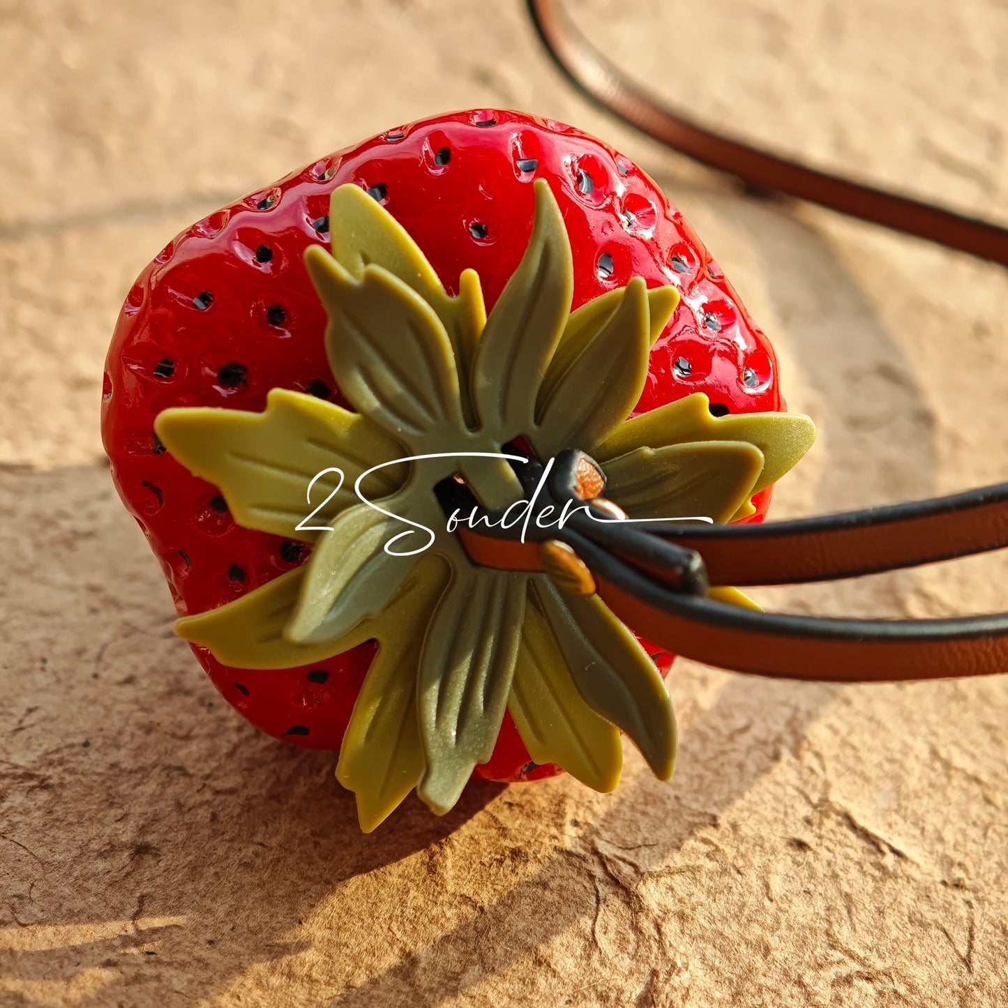 This is a simulated strawberry bag charm. The charm features a strawberry, the same size as a real strawberry, and is made of high-quality resin, giving it a very realistic appearance. It also has a leather cord attached, allowing it to be hung on bags, earphone cases, or used as a keychain. It's versatile and very cute.