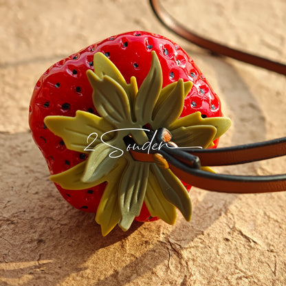 This is a simulated strawberry bag charm. The charm features a strawberry, the same size as a real strawberry, and is made of high-quality resin, giving it a very realistic appearance. It also has a leather cord attached, allowing it to be hung on bags, earphone cases, or used as a keychain. It's versatile and very cute.