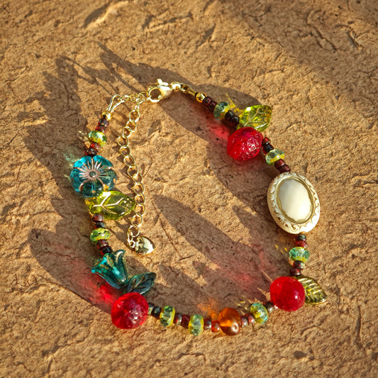 This vibrant bracelet features a colorful mix of ruby-red lemon, sapphire-blue flower, and emerald-green leaf charms, all dangling from a shimmering Czech glass bead chain.