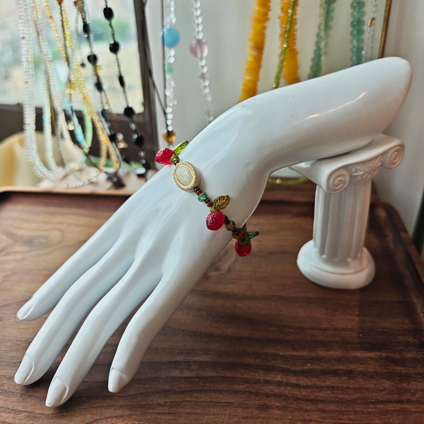This vibrant bracelet features a colorful mix of ruby-red lemon, sapphire-blue flower, and emerald-green leaf charms, all dangling from a shimmering Czech glass bead chain.