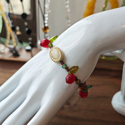 This vibrant bracelet features a colorful mix of ruby-red lemon, sapphire-blue flower, and emerald-green leaf charms, all dangling from a shimmering Czech glass bead chain.