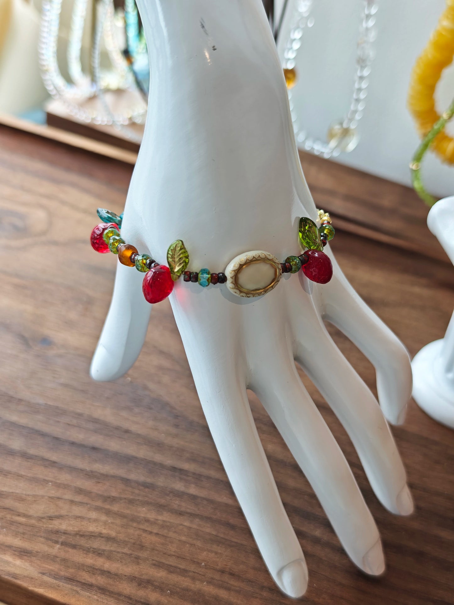 This vibrant bracelet features a colorful mix of ruby-red lemon, sapphire-blue flower, and emerald-green leaf charms, all dangling from a shimmering Czech glass bead chain.