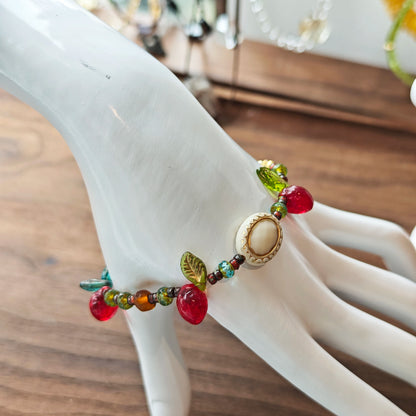 This vibrant bracelet features a colorful mix of ruby-red lemon, sapphire-blue flower, and emerald-green leaf charms, all dangling from a shimmering Czech glass bead chain.