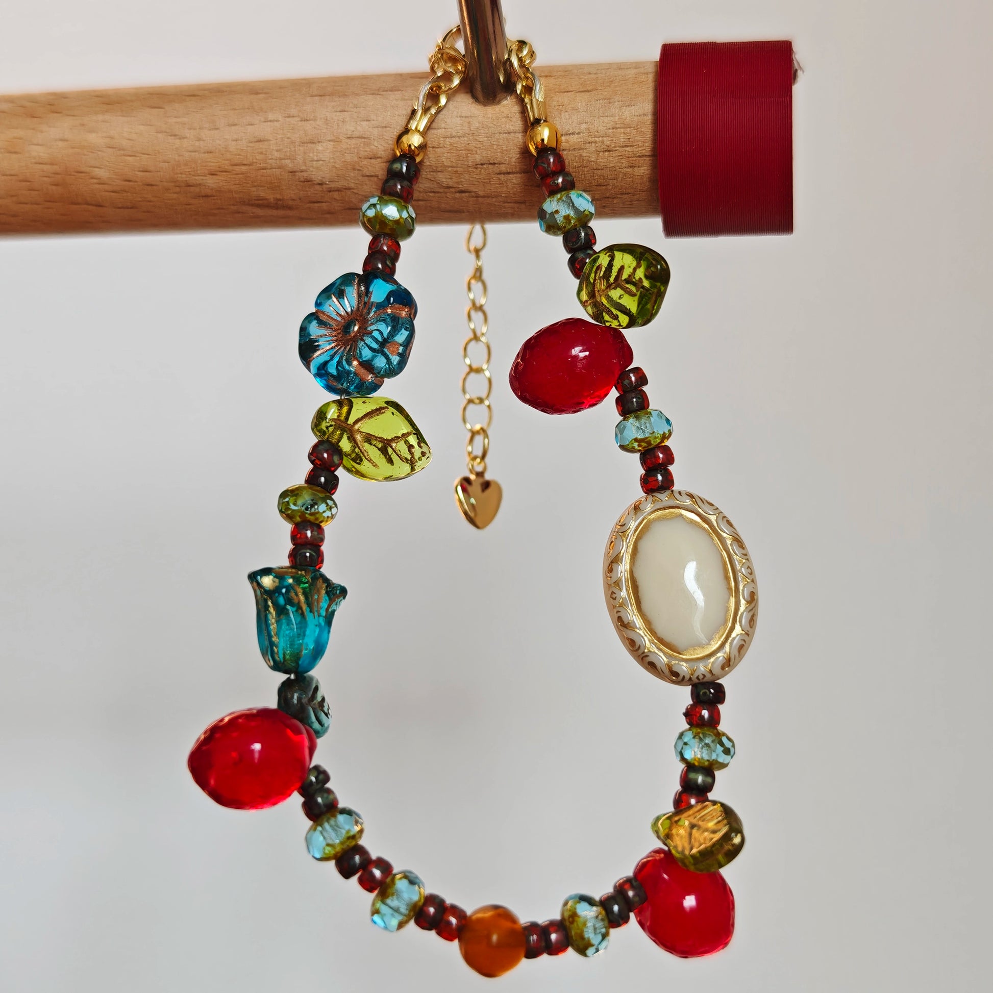 This vibrant bracelet features a colorful mix of ruby-red lemon, sapphire-blue flower, and emerald-green leaf charms, all dangling from a shimmering Czech glass bead chain.