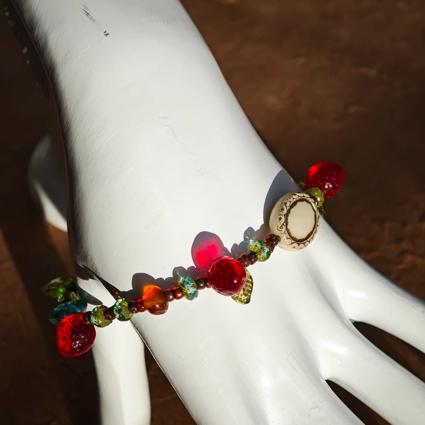 This vibrant bracelet features a colorful mix of ruby-red lemon, sapphire-blue flower, and emerald-green leaf charms, all dangling from a shimmering Czech glass bead chain.