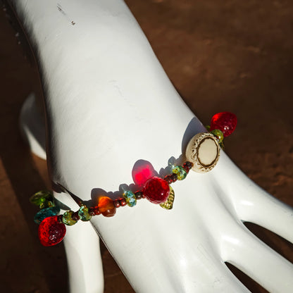 This vibrant bracelet features a colorful mix of ruby-red lemon, sapphire-blue flower, and emerald-green leaf charms, all dangling from a shimmering Czech glass bead chain.
