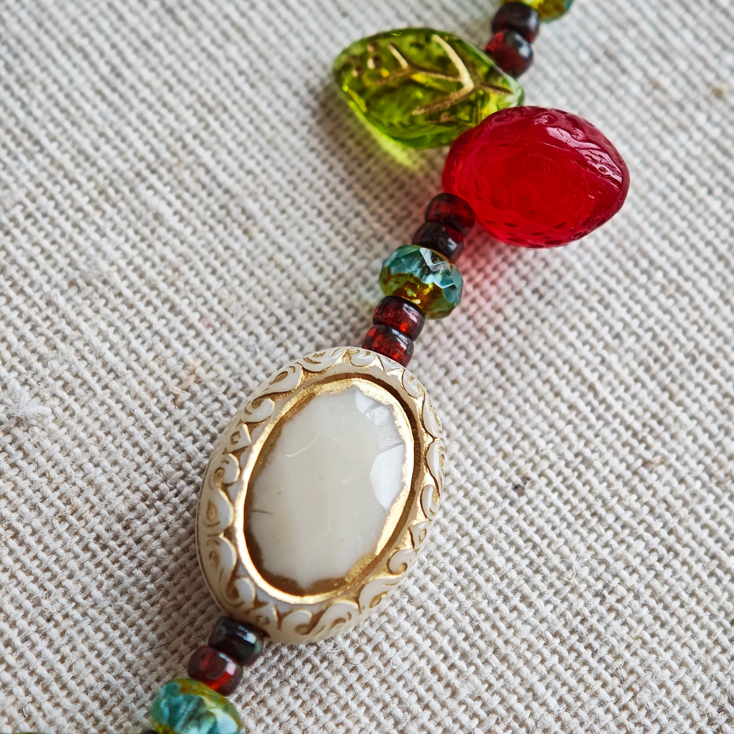 This vibrant bracelet features a colorful mix of ruby-red lemon, sapphire-blue flower, and emerald-green leaf charms, all dangling from a shimmering Czech glass bead chain.