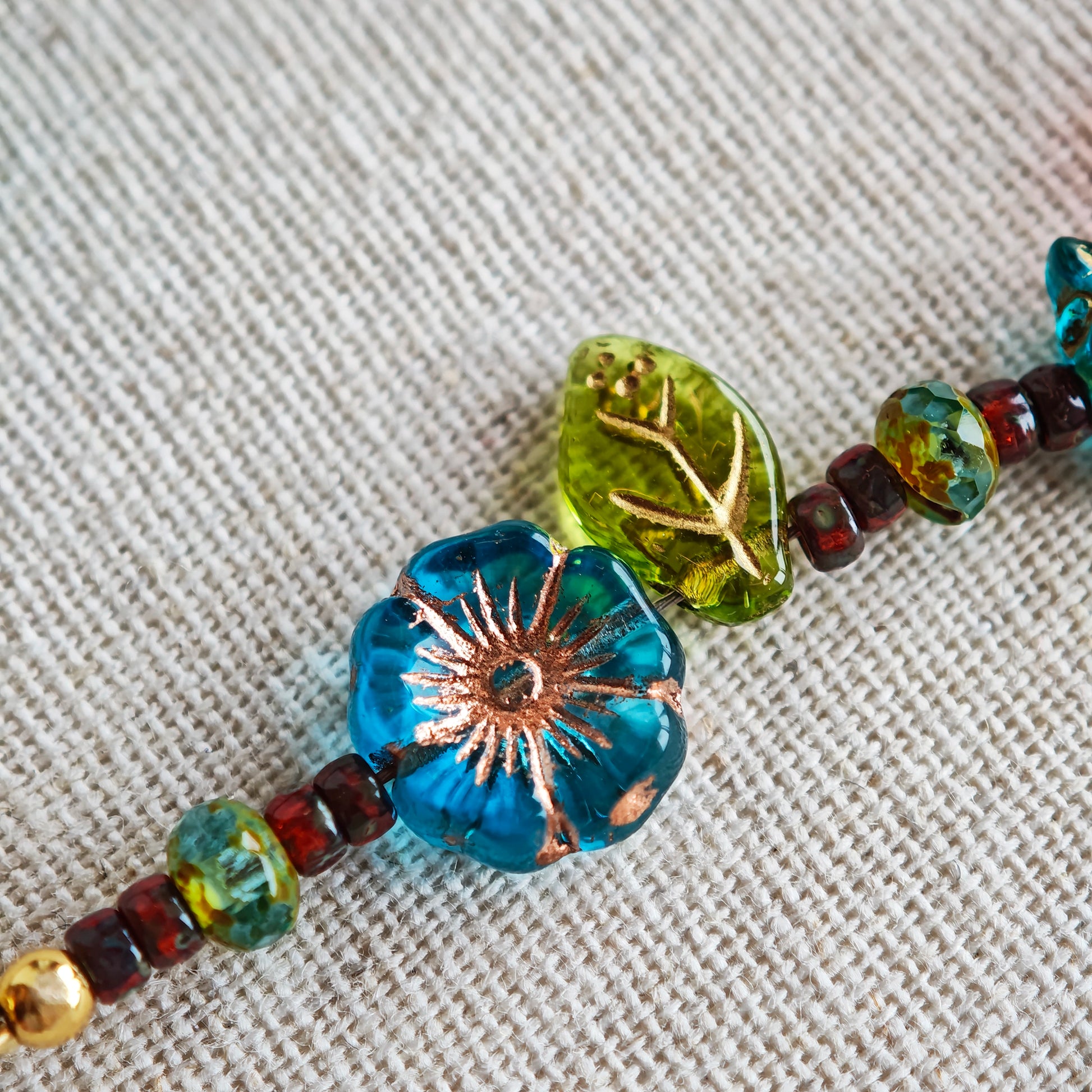 This vibrant bracelet features a colorful mix of ruby-red lemon, sapphire-blue flower, and emerald-green leaf charms, all dangling from a shimmering Czech glass bead chain.