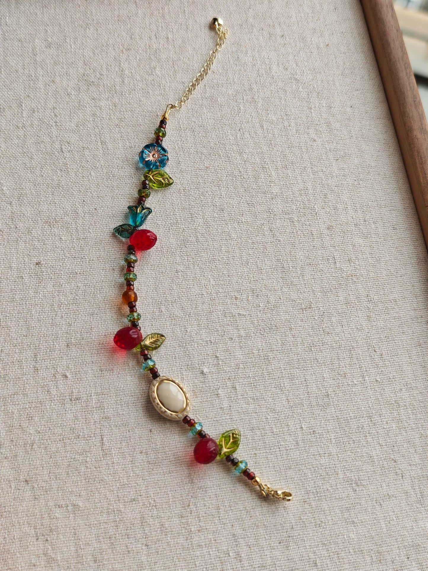 This vibrant bracelet features a colorful mix of ruby-red lemon, sapphire-blue flower, and emerald-green leaf charms, all dangling from a shimmering Czech glass bead chain.