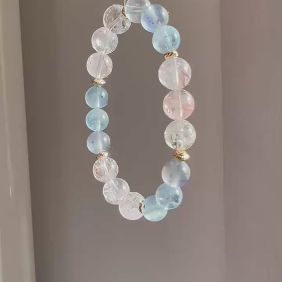 The piece unites aquamarine’s calm with rutile’s sparkle, ringed in subtle gold.